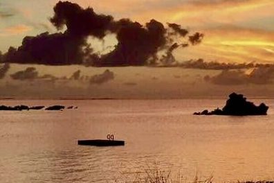 Vivid sunset over calm sea with silhouetted rocks and colorful clouds.