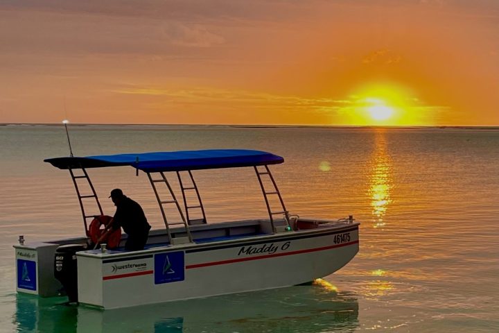 Boat on calm water at sunset with a vibrant orange sky.