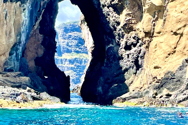 Rock archway above bright blue ocean water under clear sky.