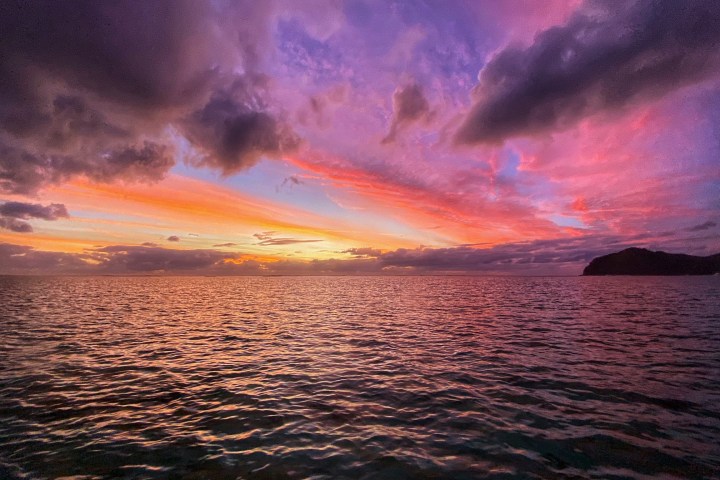 Vibrant sunset over ocean with colorful sky and a silhouetted island on the horizon.